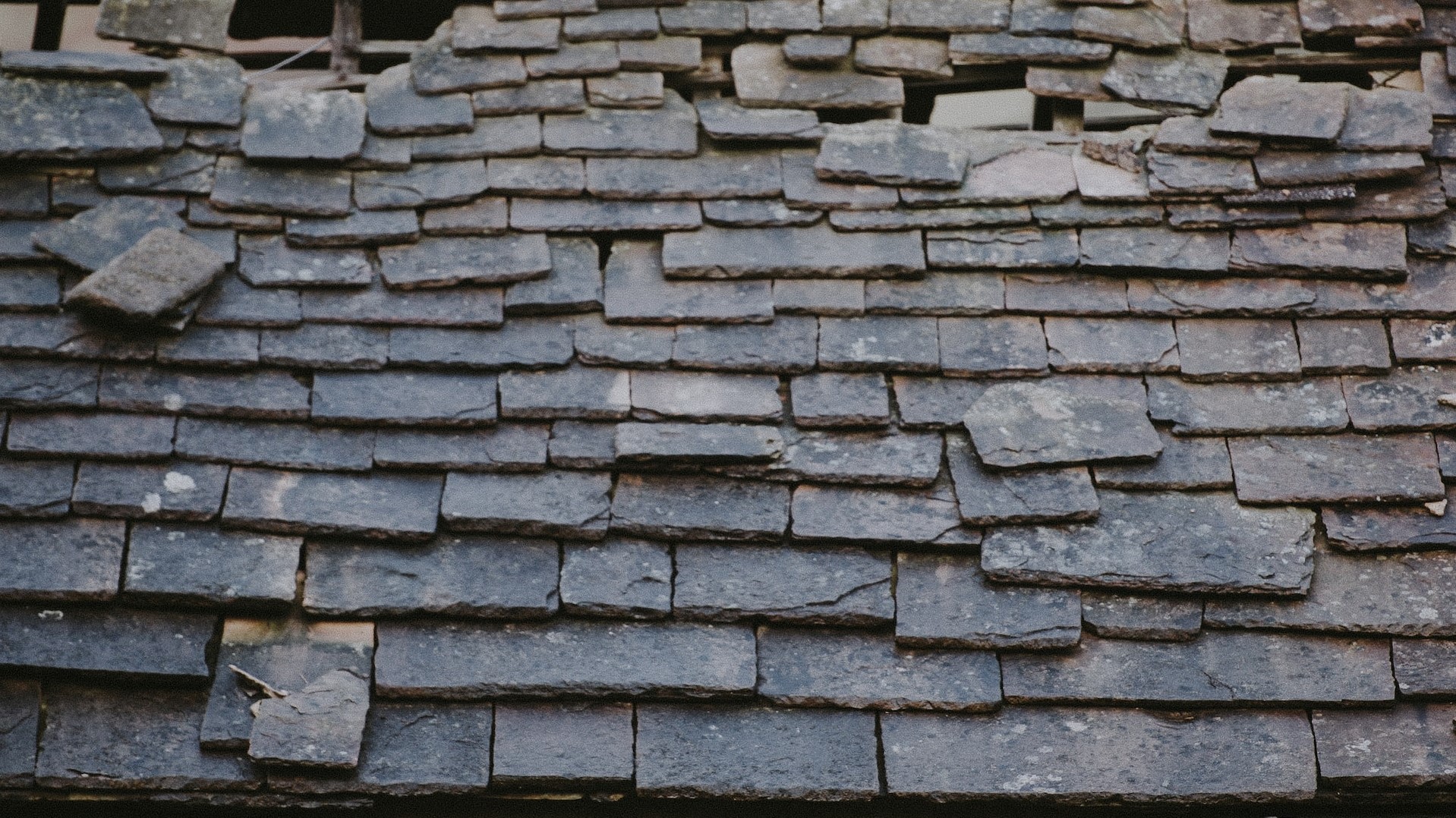 A roof with broken and missing shingles.