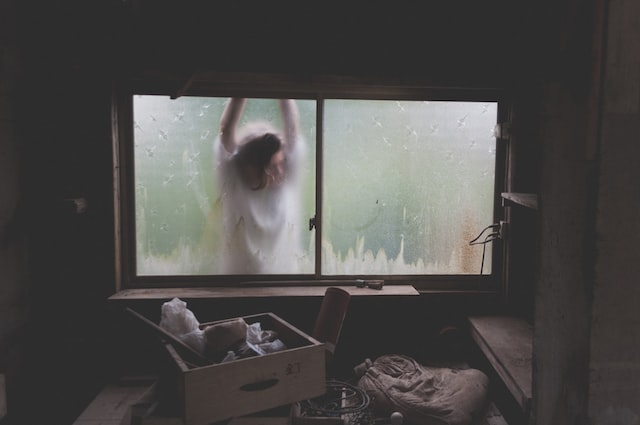 Woman stands on basement window looking at stored stuff.